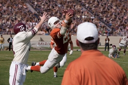 A football player in an orange jersey jumps to throw a ball while a defender in white reaches for him.