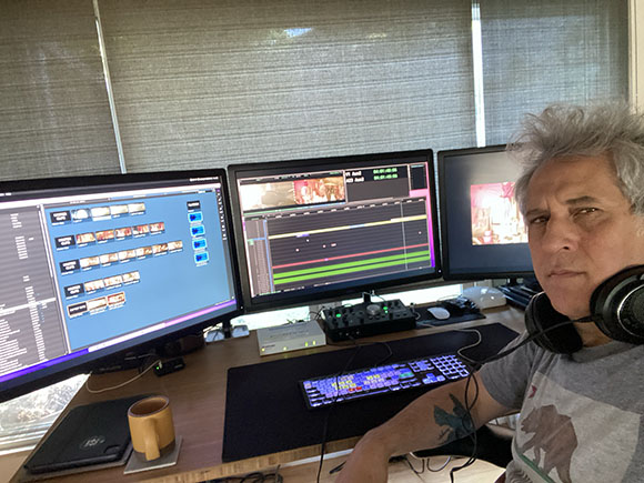 A man sits in front of a three-monitor workstation displaying video editing software.