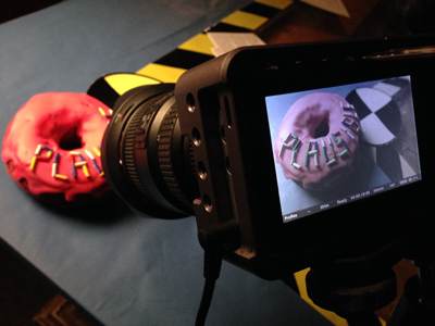 A professional camera filming a pink donut with the word 'PLAY' written in colorful letters.