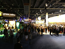 Crowds of people walking through a large, dimly lit convention center with various illuminated vendor booths.