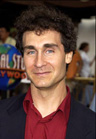 A man with dark curly hair and blue eyes wearing a red shirt and dark blazer.
