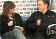 A woman and a man sit side-by-side holding microphones during an interview.