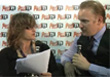A woman holding papers looks toward a man holding a microphone during an interview.