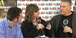A woman speaking into a microphone while two men listen during an interview setting.