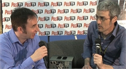 Two men in blue shirts sit facing each other holding microphones against a Post TV backdrop.