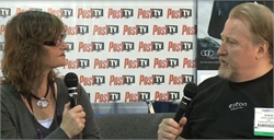 A woman with glasses holds a microphone while interviewing a man in a black shirt.