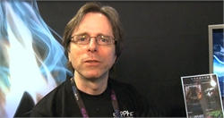A man with brown hair and glasses wearing a black shirt and a lanyard.