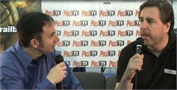 Two men sit facing each other, each holding a microphone, in front of a white backdrop with PostTV logos.
