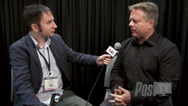 A man in a blue blazer holds a microphone toward a man in a black shirt during an interview.