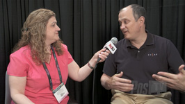 A woman in a pink shirt holds a microphone toward a man in a dark polo shirt during an interview.