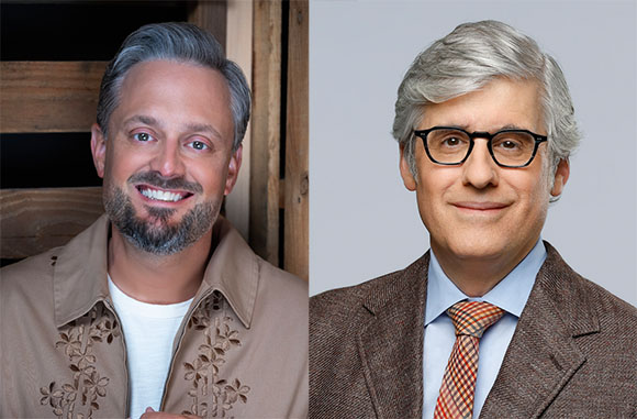 Two men smiling; one with a beard in a tan shirt, the other with gray hair and glasses in a brown suit.