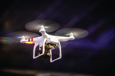 A white quadcopter drone with spinning propellers flying in a dark environment.