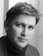 Black and white close-up portrait of a man with wavy hair looking toward the camera.