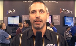 A man with short dark hair and a goatee speaks into a microphone in front of a RAID and Archive display.