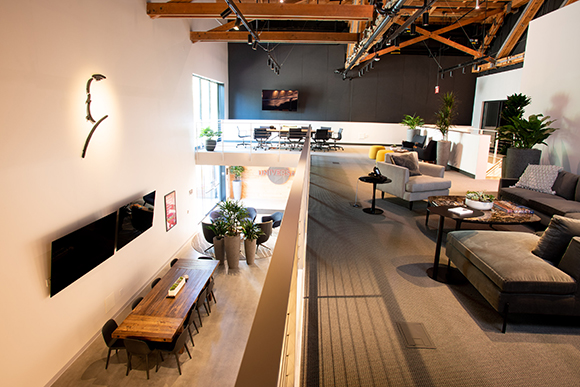 A multi-level modern office featuring a lounge with sofas and a lower level with a long wooden table.