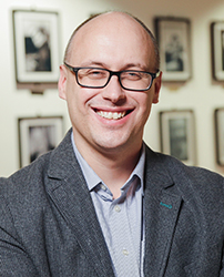 A man wearing glasses and a suit jacket smiles.
