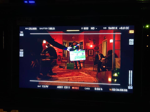 A film set monitor shows a scene with actors, a clapperboard, and camera settings displayed.