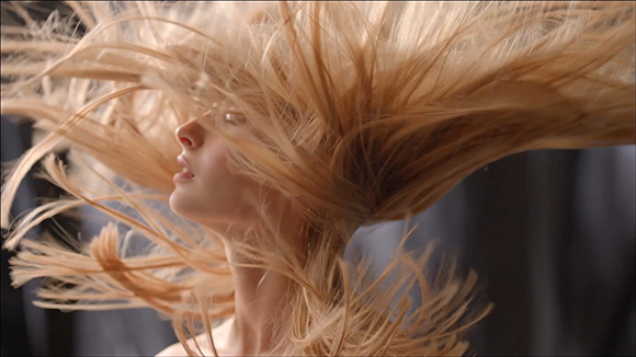Long blonde hair blowing upward and outward in a dynamic, wind-swept motion against a dark background.