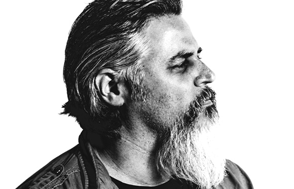 Black and white profile portrait of a man with slicked-back hair and a long, light-colored beard.