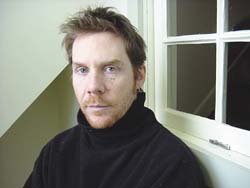A man with light brown hair and a beard wearing a black turtleneck, looking forward.