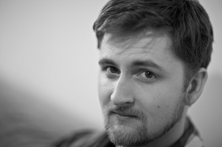 Black and white close-up portrait of a man with short hair and a beard looking toward the camera.