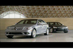 A silver Mercedes-Benz sedan in the foreground and a black sedan behind it in a large hall.