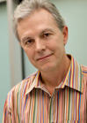 A man with graying hair wearing a colorful vertical striped shirt.