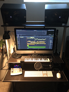 A computer monitor displaying music software, flanked by two large speakers, a MIDI keyboard, and a white keyboard.