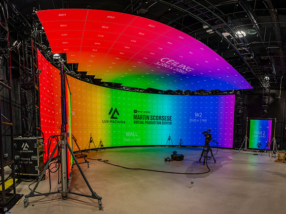 A professional film studio featuring large, curved LED screens displaying colorful gradients.
