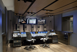 A professional recording studio featuring large mixing consoles, two ergonomic chairs, and multiple computer monitors.