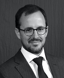 Black and white headshot of a man with glasses, a beard, and a suit and tie.