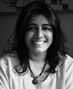 Black and white headshot of a smiling woman with dark hair wearing a necklace.