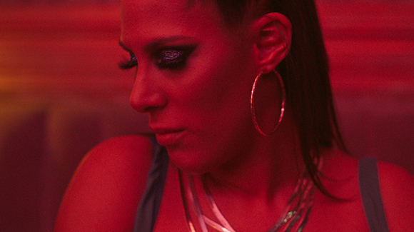 A woman in profile wearing large hoop earrings and dark eye makeup under intense red light.