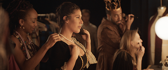 People in a dressing room applying makeup and adjusting costumes.