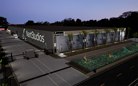 A large, modern gray industrial building with NantStudios signage and palm trees at twilight.