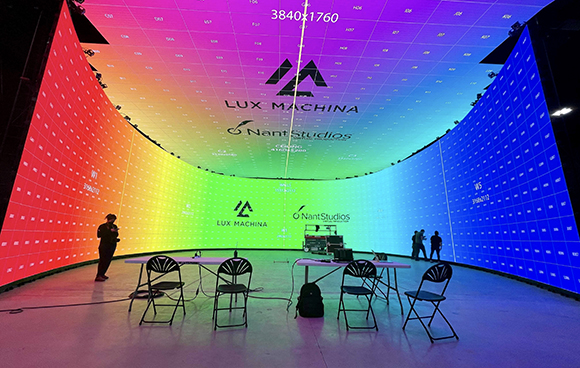 A massive, curved digital screen displaying a rainbow gradient and logos in a dark studio setting.