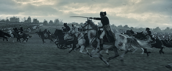 Soldiers on horseback charging across a field with swords drawn under a cloudy sky.