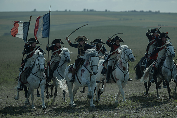 Soldiers in 18th-century military uniforms riding white horses across a grassy field.