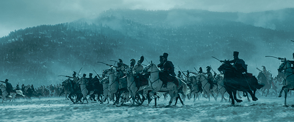 Mounted figures in dark clothing ride through a vast, snowy landscape under a heavy, overcast sky.