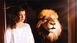 A young girl in a white shirt looks toward a large lion's head displayed in a dark room.
