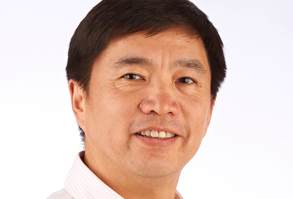 A smiling middle-aged man with short dark hair looking toward the camera against a white background.