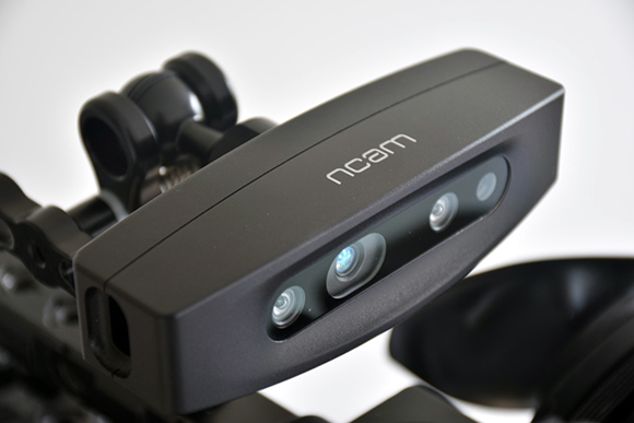 A black ncam sensor device with three lenses mounted on a camera rig against a white background.