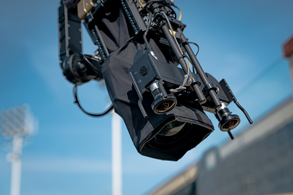A black cinema camera with a large lens attached to a mechanical robotic arm under a clear blue sky.