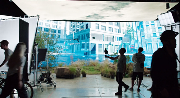 Film crew working on a set with a large blue screen and city backdrop.