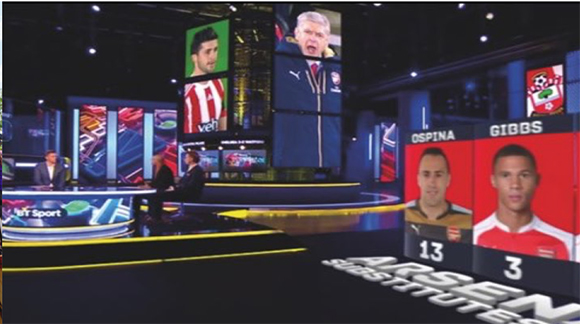 A dark sports broadcast studio with large digital screens displaying soccer players and presenters.