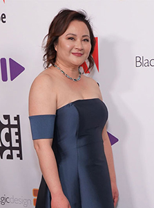 A woman with brown hair wearing a blue strapless gown and a teal necklace.