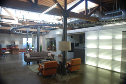Industrial loft interior with exposed wooden beams, metal pipes, and a large glowing glass block wall.