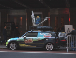 A dark car with NewTek and Canon branding, equipped with a large satellite dish on its roof.