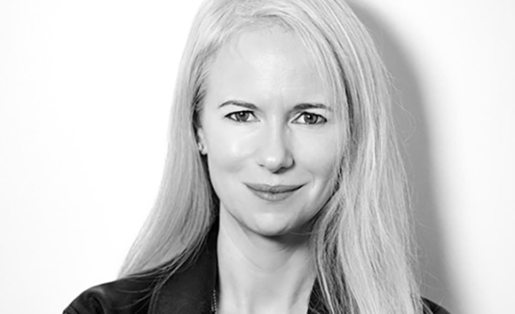 Black and white headshot of a woman with long, light-colored hair looking toward the camera.