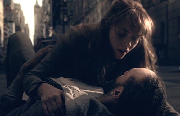 A woman leans over a man lying on a city street during twilight.